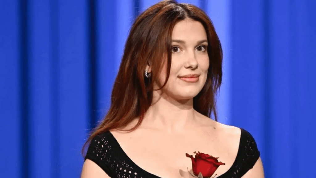 Millie Bobby Brown sheer black knit catsuit, Millie Bobby Brown naked dressing Tonight Show, Millie Bobby Brown braless fashion statement, Millie Bobby Brown auburn hair transformation, Millie Bobby Brown Stranger Things Season 5 press circuit, Millie Bobby Brown crochet knit jumpsuit look, Millie Bobby Brown girly goth naked dress style, Millie Bobby Brown Bronx Banco Liora gown fishnet, Millie Bobby Brown daring red carpet outfits 2025, Millie Bobby Brown lingerie inspired fashion trend